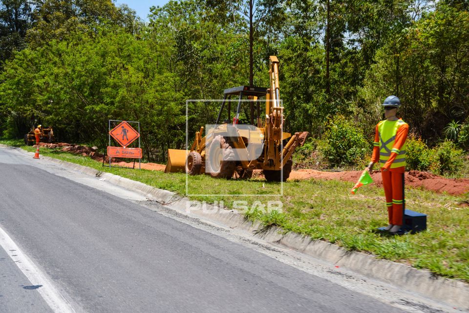 Boneco sinalizador de obras e retroescavadeira na margem da rodovia