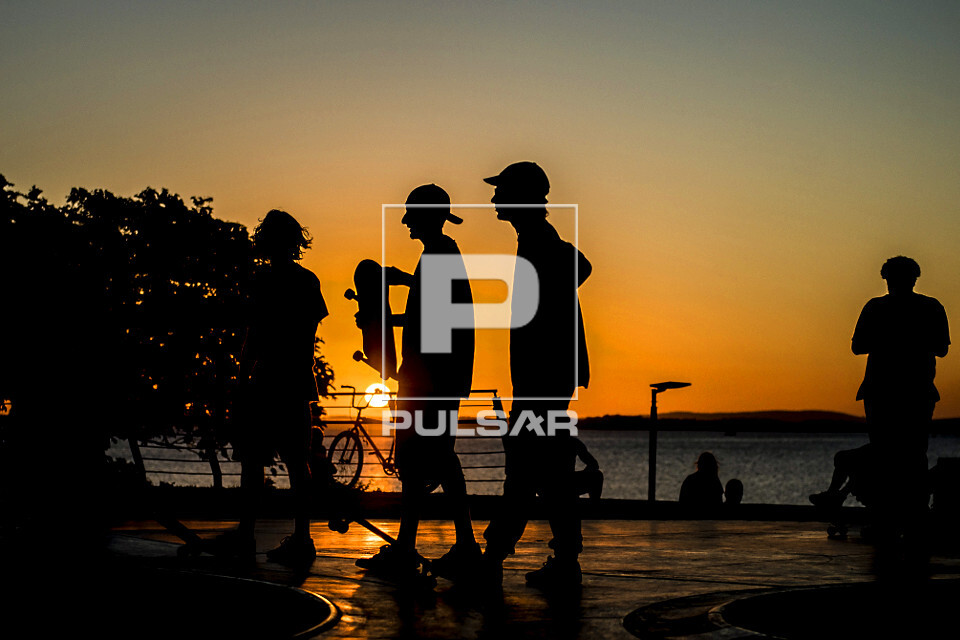 Jovens em pista de skate com o pôr do sol na orla do Rio Guaíba - 