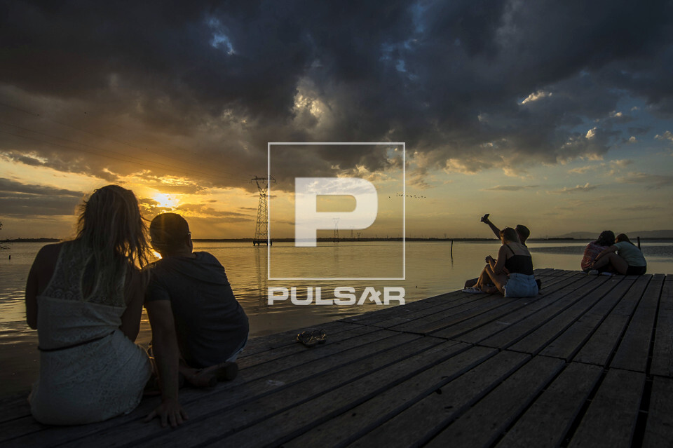 Pessoas observam paisagem do pôr do sol no rio Tramandaí