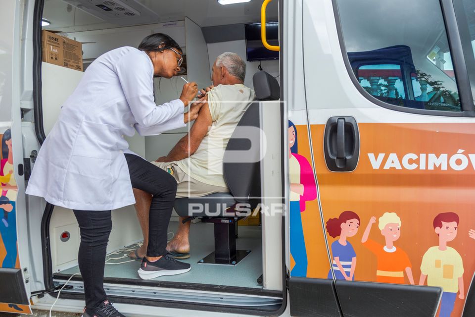 Enfermeira vacinando homem durante campanha contra covid e gripe dentro de veículo Vacimóvel na Praça Antô