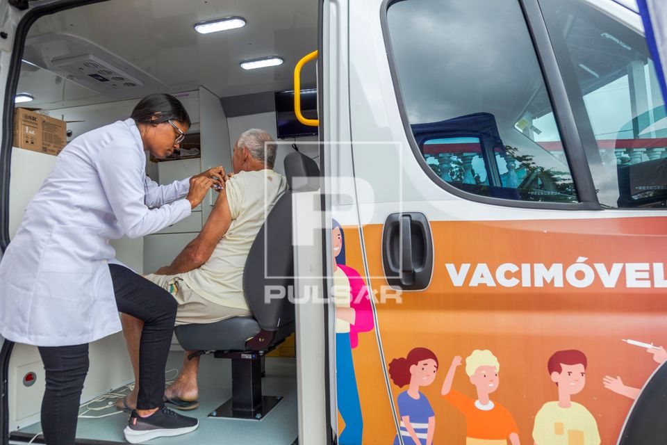 Enfermeira vacinando homem durante campanha contra covid e gripe dentro de veículo Vacimóvel na Praça Antô