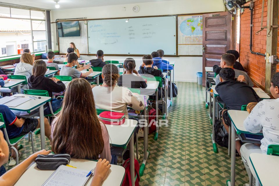 Professora fazendo chamada de presença de alunos em sala de aula