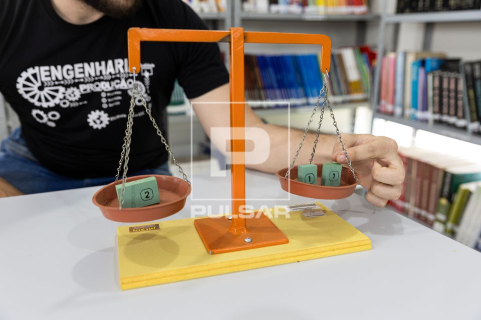 Estudante usa balança de pratos para comparação entre o peso e a massa de diferentes objetos