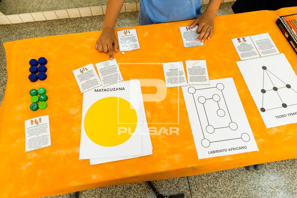 Aluno interagindo com jogos de tabuleiro de origem africana na Semana da Consciência Negra na Escola Municipa