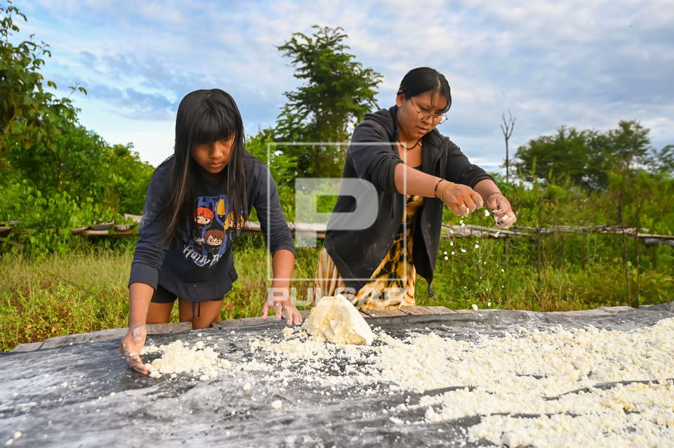 Indígena Waurá e filha esfarelando o polvilho para secar ao sol no jirau - Parque Indígena do Xingu