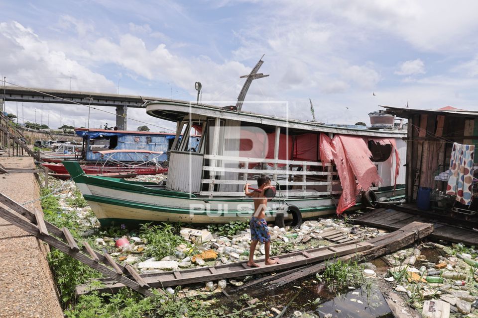 Menino atravessando pinguela sobre o rio Negro com lixo acumulado