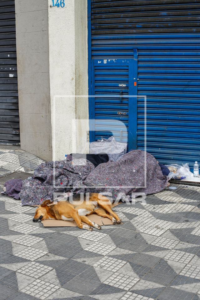 Moradores de rua e cão dormindo na calçada no centro da cidade