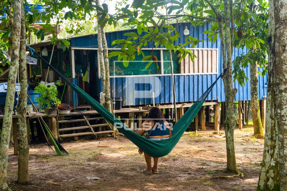 Mulher descansando em rede em frente à moradia - palafita