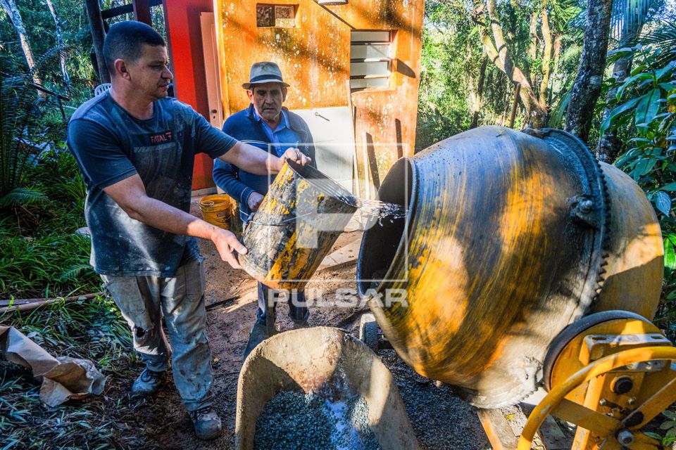 Pedreiro colocando água na betoneira para fazer concreto em obra residencial em área de mata atlântica