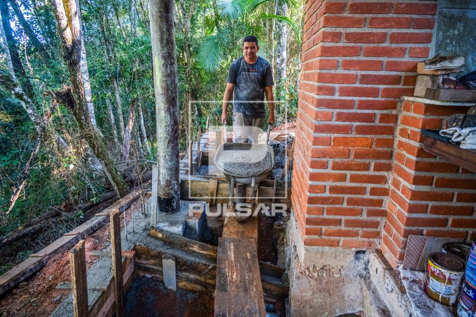 Pedreiro levando concreto pronto na carriola para fazer obra residencial em área de mata atlântica
