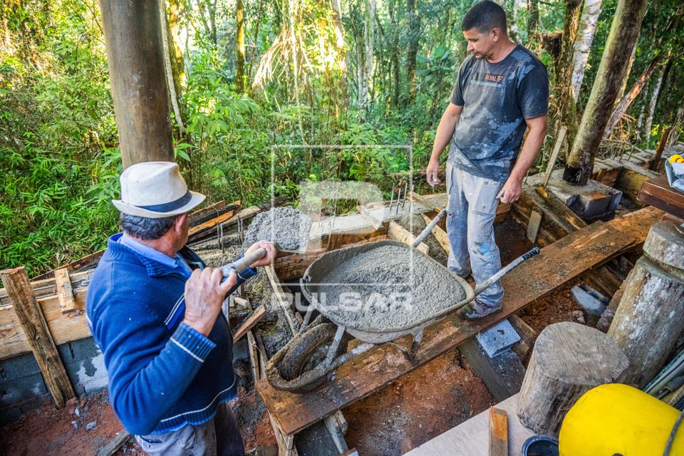 Pedreiro usando pá para preencher com cimento formas de madeira ou caixaria durante obra residencial