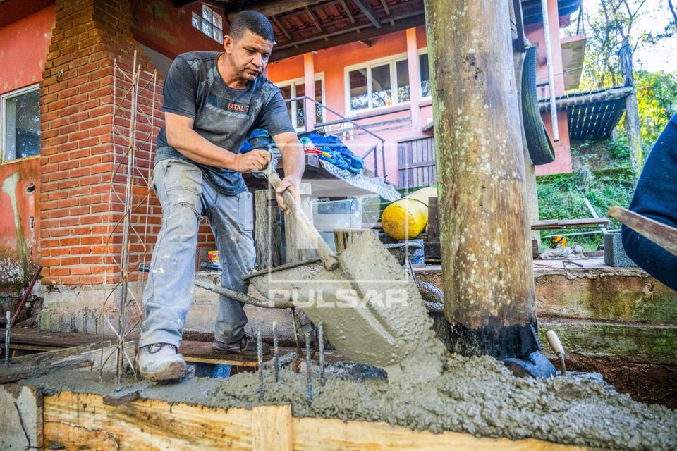 Pedreiro usando pá para preencher com cimento formas de madeira ou caixaria durante obra residencial
