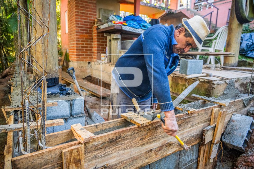 Pedreiro batendo com martelo na forma de madeira ou caixaria para assentar concreto em obra residencial