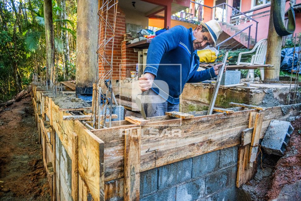 Pedreiro usando pá de pedreiro para assentar concreto na forma de madeira ou caixaria durante obra residencia