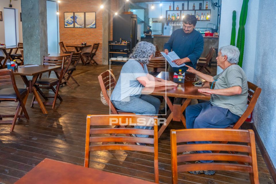 Vista interna de restaurante de comida japonesa com chef de cozinha mostrando cardápio para clientes
