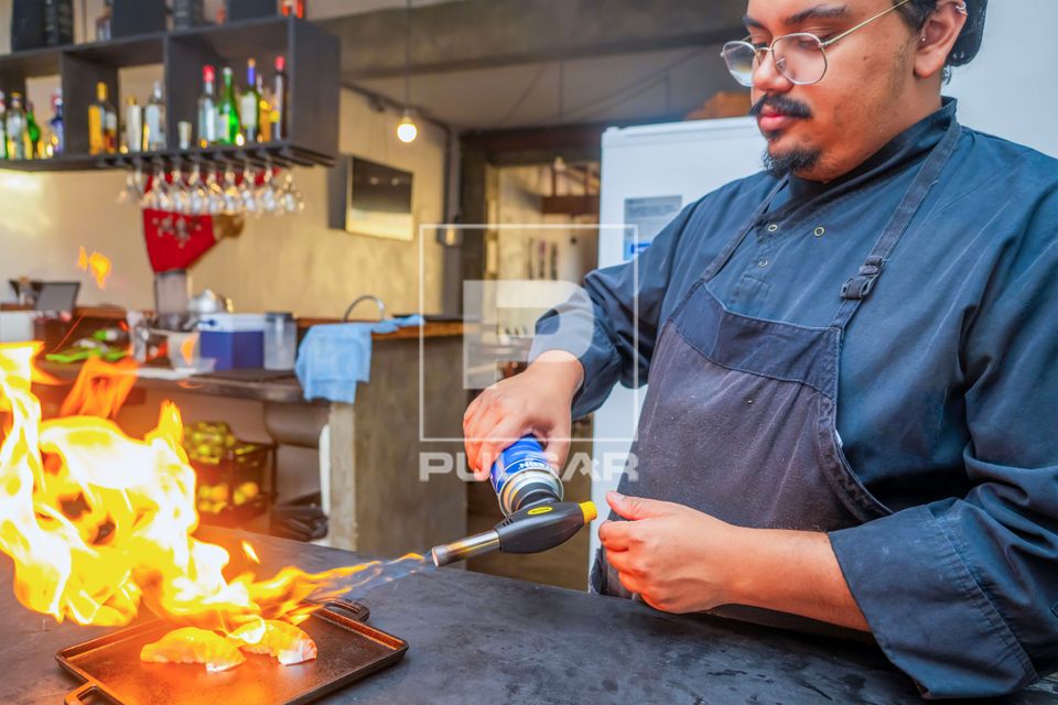 Chef de cozinha e proprietário de restaurante de comida japonesa flambando sashimi de Salmão com maçarico c