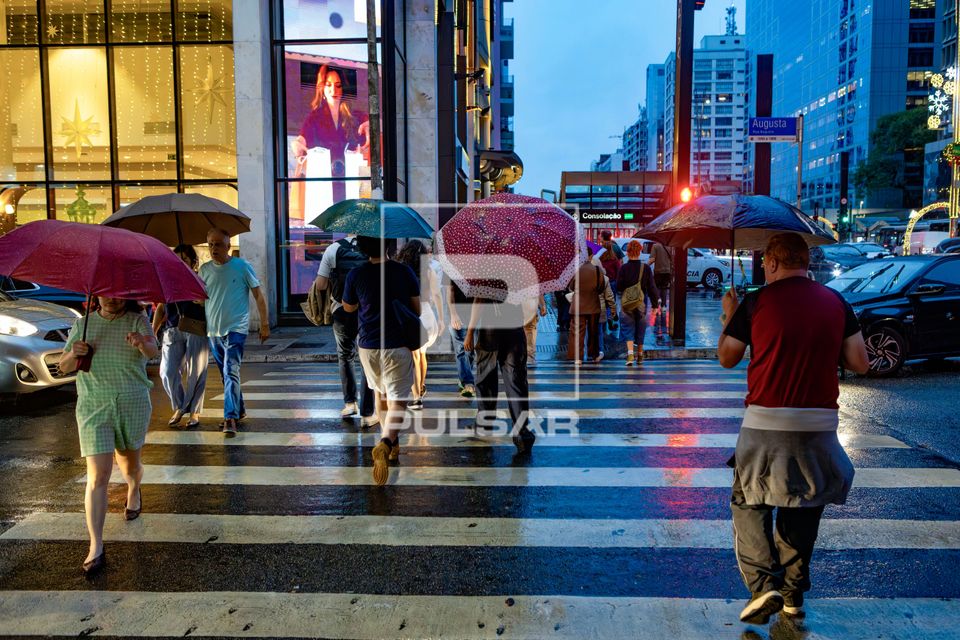 Pessoas atravessando faixa de pedestre na Rua augusta com guarda-chuvas em noite de chuva