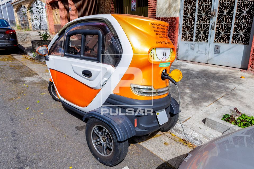 Microcarro elétrico de três rodas sendo recarregado em ponto 