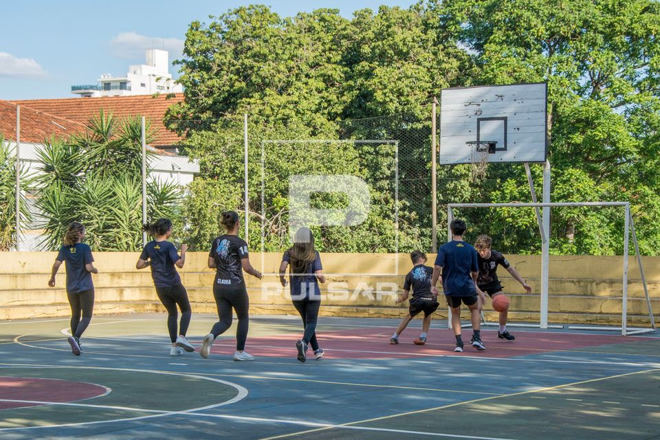 Alunos jogando basquete em quadra durante aula de educação física