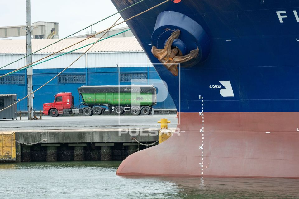 Navio de carga atracado e ao fundo caminhão transportando carga no Complexo Portuário de Paranaguá