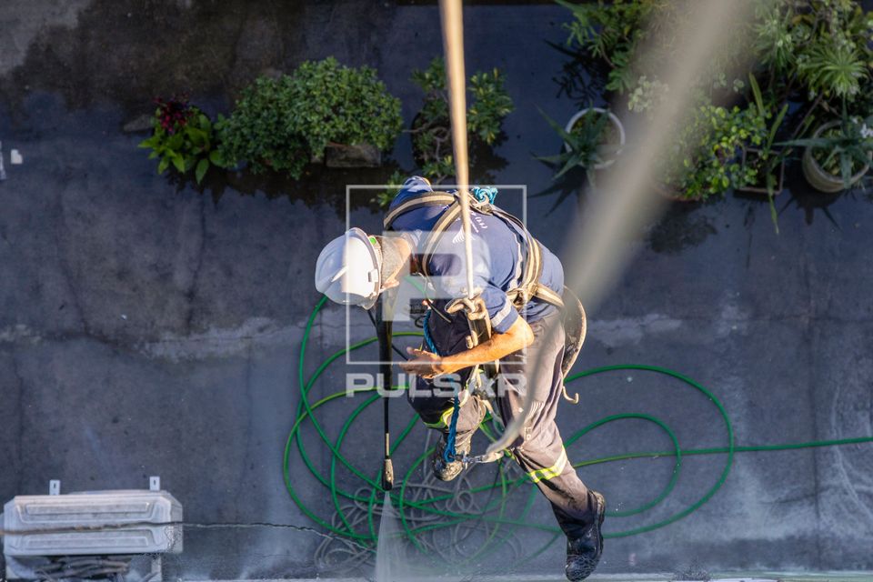 Trabalhador usando equipamento de EPI e rapel para limpar fachada de prédio residencial