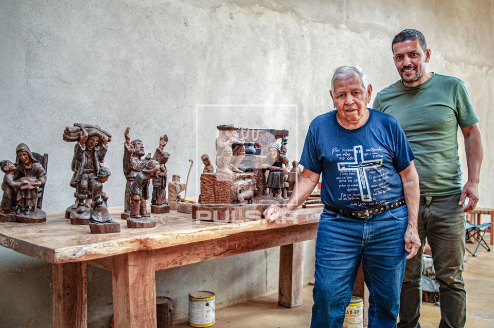 Retrato de artesão e filho posando juntos ao lado de esculturas feitas em madeira