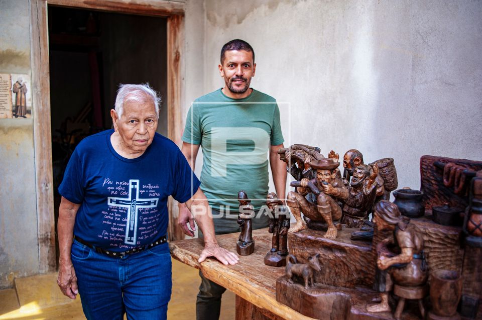 Retrato de artesão e filho posando ao lado de esculturas feitas em madeira