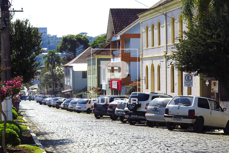 Casas com arquitetura típica italiana e veículos estacionados em rua com declive no centro da cidade - 
