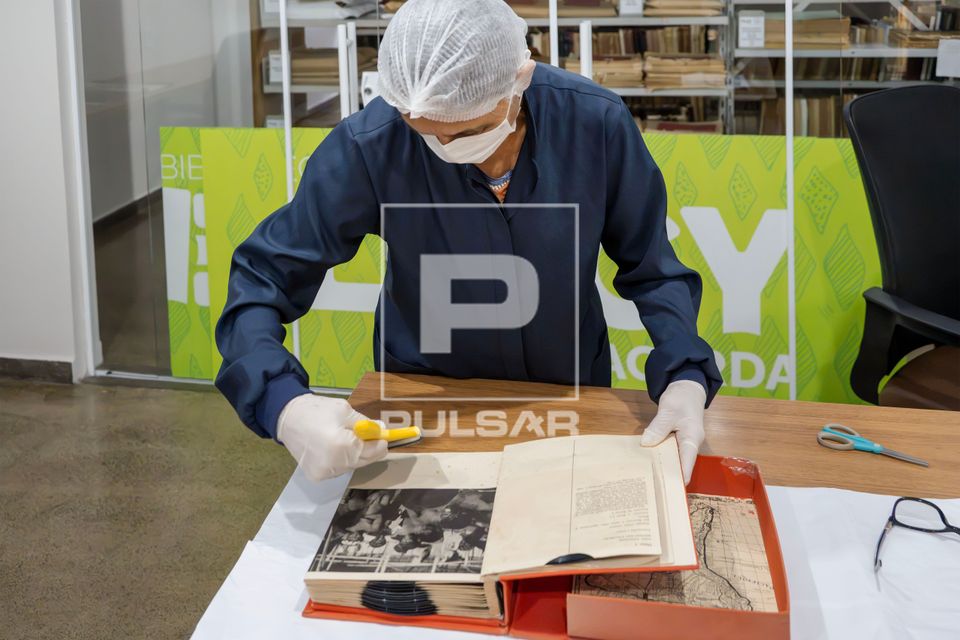 Trabalhadora do Setor de Obras Raras da Biblioteca Pública Estadual Elcy Lacerda fazendo limpeza em livro