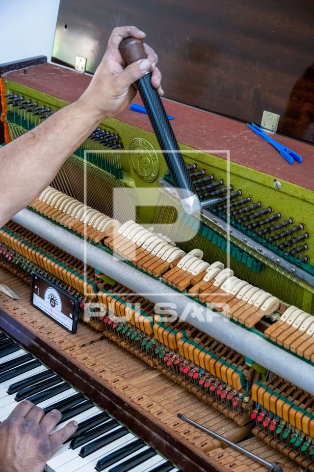 Profissional afinando piano de parede usando afinador digital no telefone celular