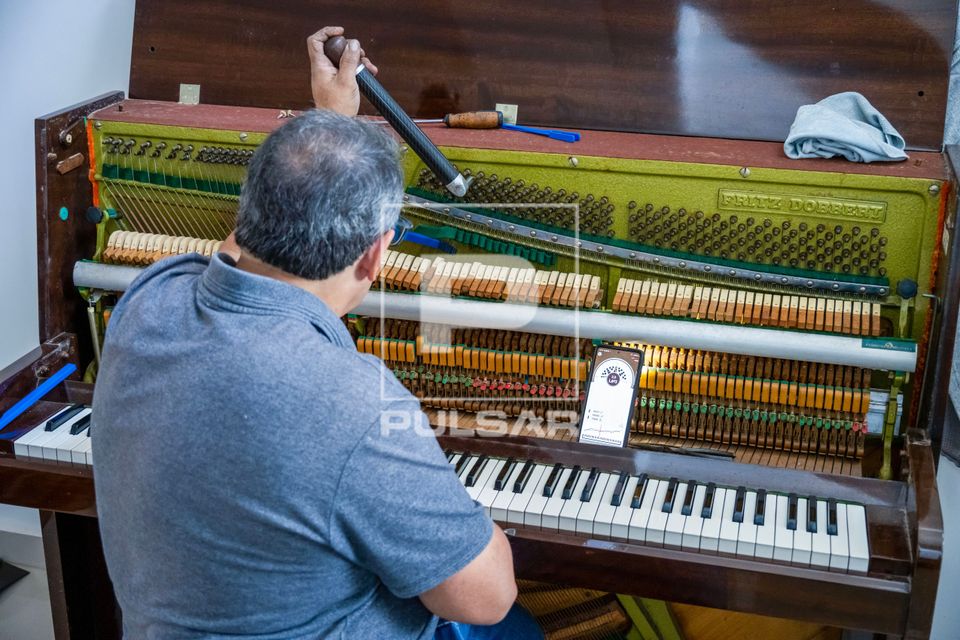 Profissional afinando piano de parede usando afinador digital no telefone celular