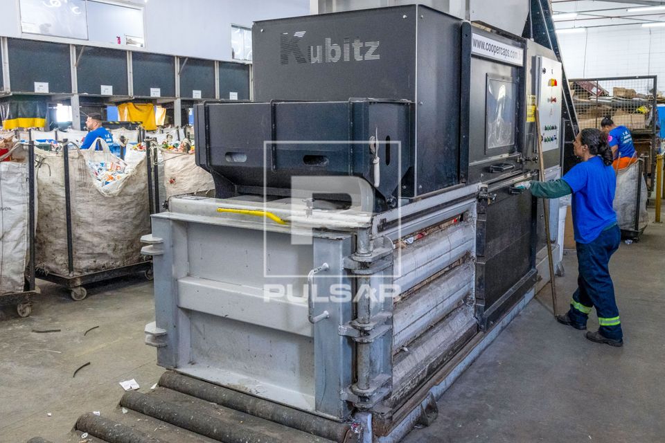 Cooperada acionando prensa enfardadeira para compactação de material reciclável em cooperativa de catadores