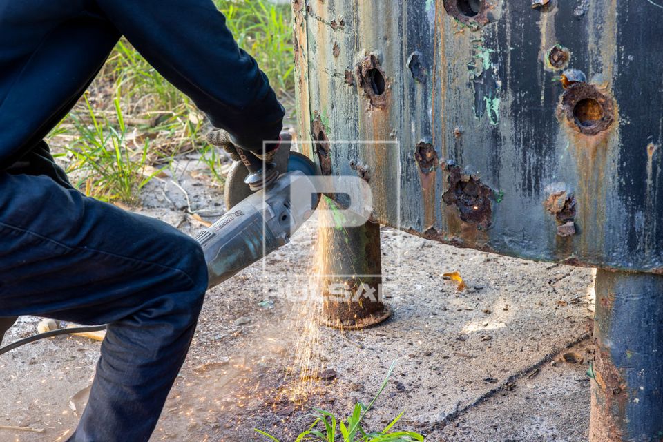 Serralheiro cortando chapa metálica de caldeira industrial com esmerilhadeira