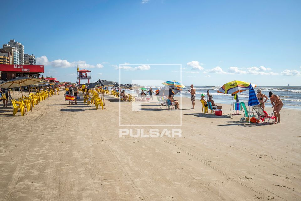 Pessoas na praia em dia ensolarado - ao fundo posto de guarda-vidas