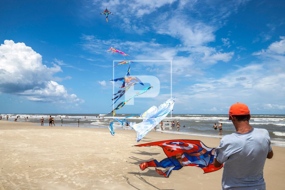 Praia com vendedor de pipas e banhistas ao fundo