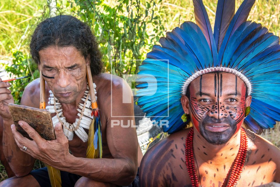 Indígenas da etnia Pataxó fazendo pintura corporal e usando cocar de penas de arara durante o evento Maricá