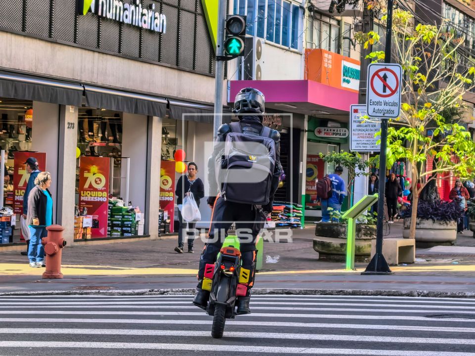 Entregador de aplicativo de comida com monociclo elétrico atravessando rua no calçadão - centro da cidade