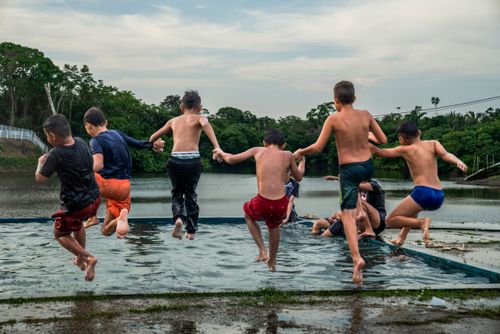 Meninos brincam em piscina de balneário com Rio Manaquiri - ao fundo