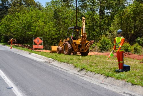 Boneco sinalizador de obras e retroescavadeira na margem da rodovia