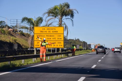 Trabalhador sinaliza equipe trabalhando no acostamento da SP-160 Rodovia dos Imigrantes
