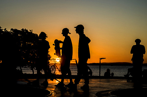 Jovens em pista de skate com o pôr do sol na orla do Rio Guaíba - 