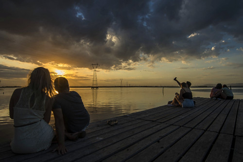 Pessoas observam paisagem do pôr do sol no rio Tramandaí