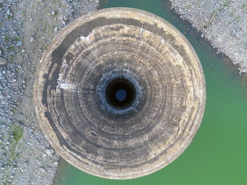 Vista de drone do vertedouro tulipa da barragem de Caconde com reservatório em nível baixo em período de es