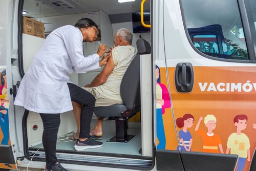 Enfermeira vacinando homem durante campanha contra covid e gripe dentro de veículo Vacimóvel na Praça Antô