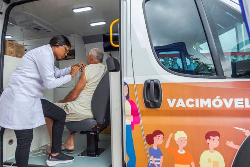 Enfermeira vacinando homem durante campanha contra covid e gripe dentro de veículo Vacimóvel na Praça Antô