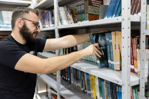 Estudante de escola técnica retirando livro de Estatística da biblioteca escolar
