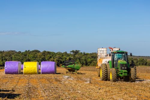 Trator puxando carreta com reservatório de água contra incêndios e à esquerda fardos de algodão recém co