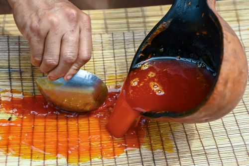 Indígena Wauja separando óleo da massa de pequi derretido na caldeirão e colocando para coar - Parque Indí