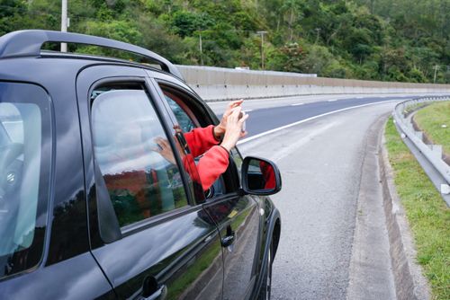 Mulher fotografa a paisagem da Rodovia dos Tamoios SP-099 de dentro de um veículo
