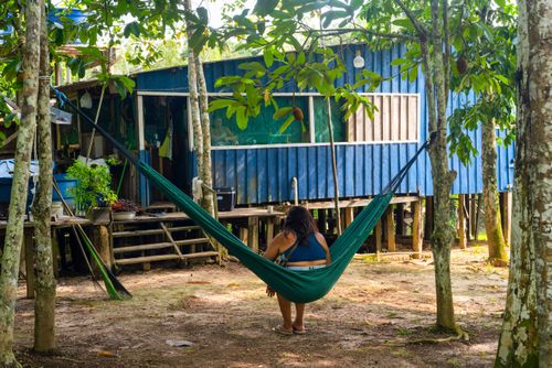 Mulher descansando em rede em frente à moradia - palafita